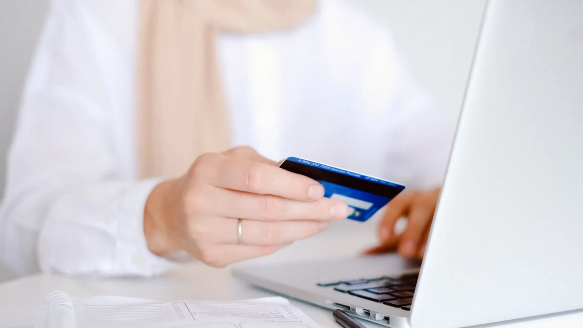 A person holding a credit card while using a laptop for online shopping, illustrating buy iptv subscription