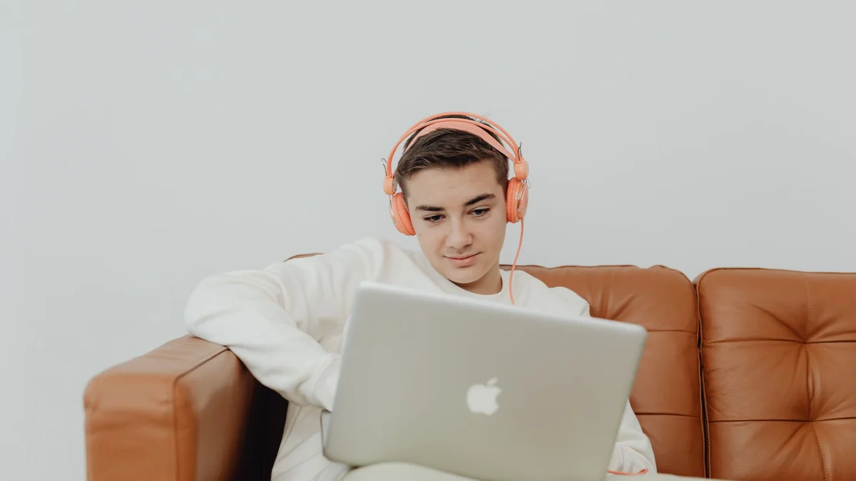 Young man sitting on a couch using a laptop with headphones, enjoying music indoors, illustrating tivimate windows